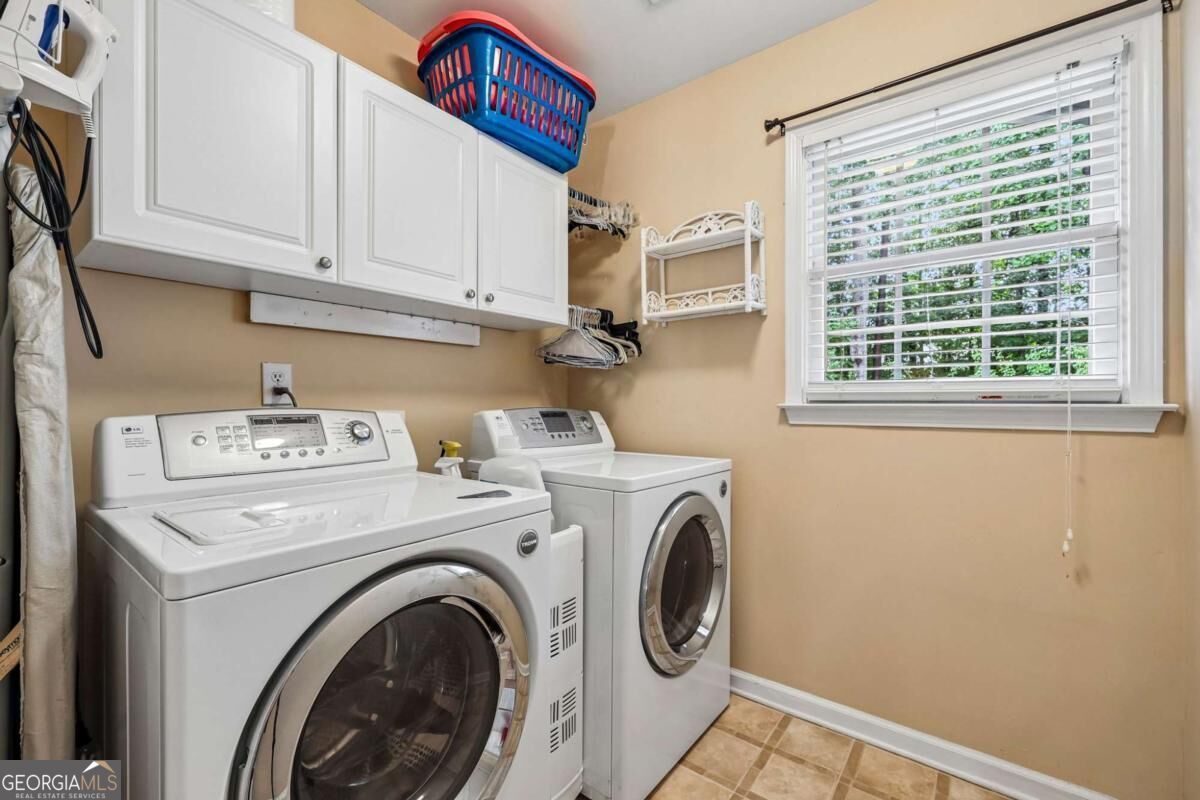 Laundry room with front-loading washer and dryer, white cabinets, and a window with blinds.