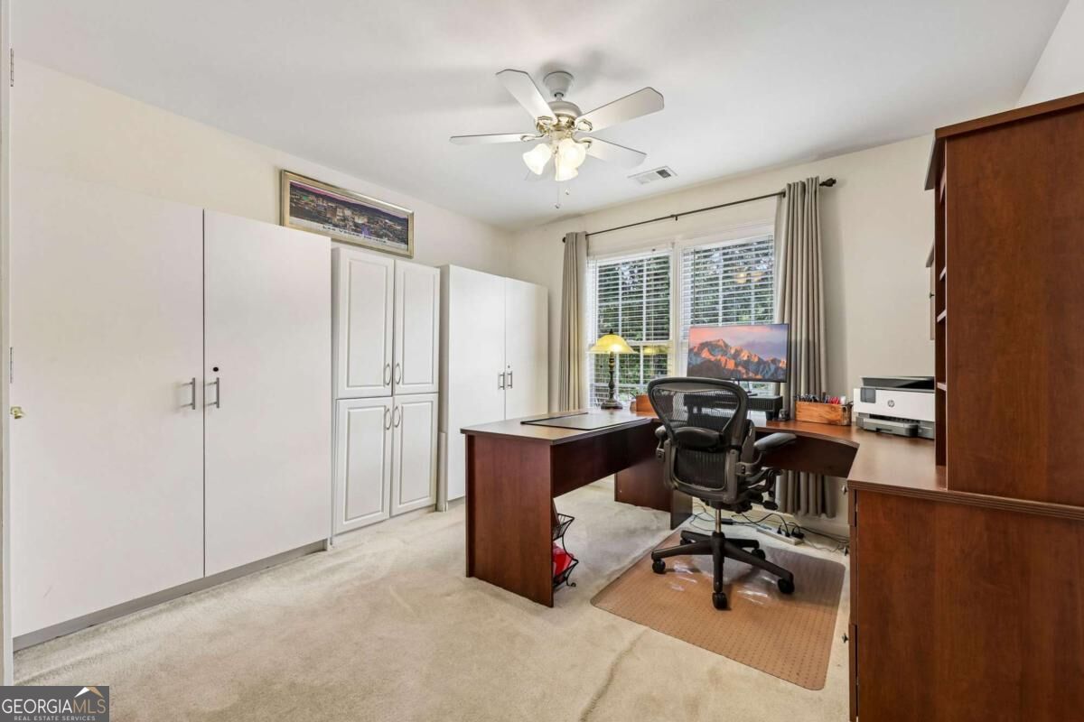 Furnished home office with built-in cabinets, an L-shaped desk, and a window overlooking greenery.