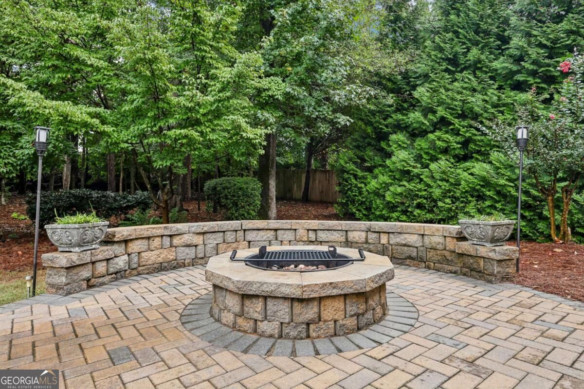 Stone patio with a circular fire pit, curved retaining wall, and mature trees.