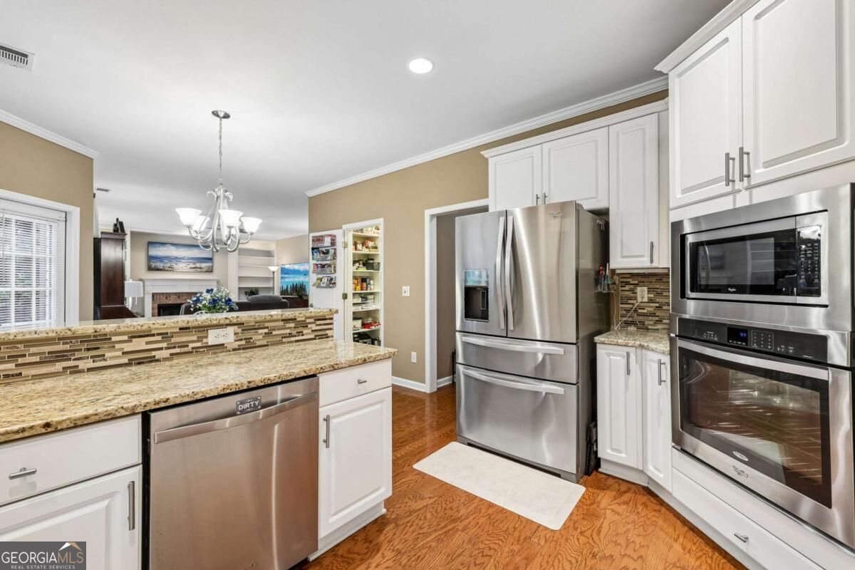 Kitchen with white cabinets, granite counters, stainless steel appliances, and a mosaic tile backsplash.