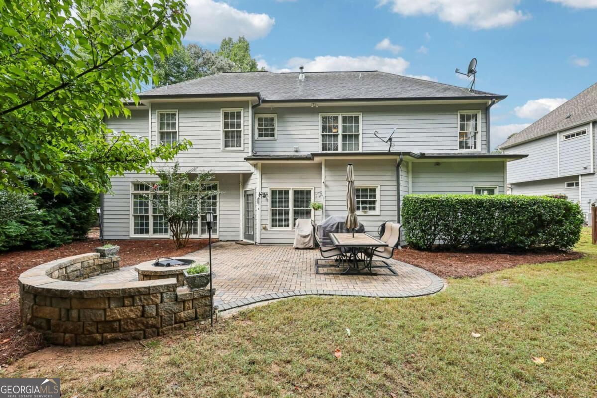 Rear of a two-story gray house with a paver patio and circular stone fire pit.