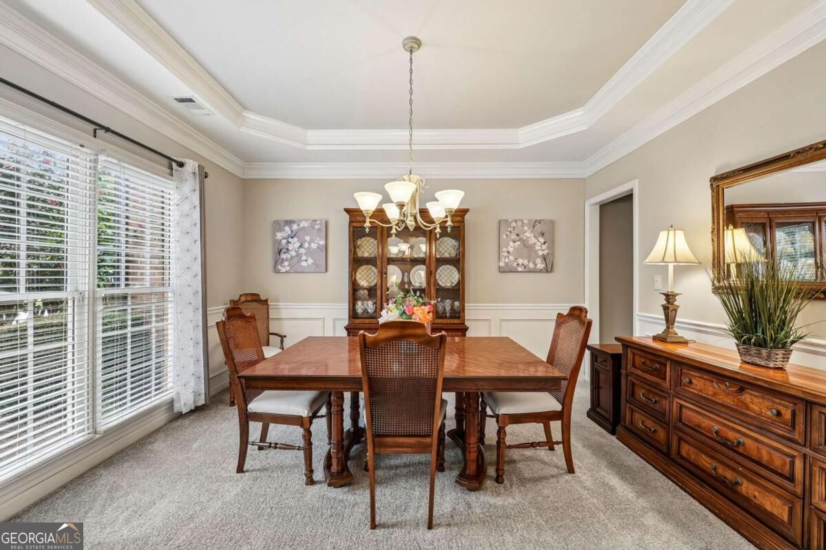 Dining room with a wooden table, china cabinet, tray ceiling, and large windows.