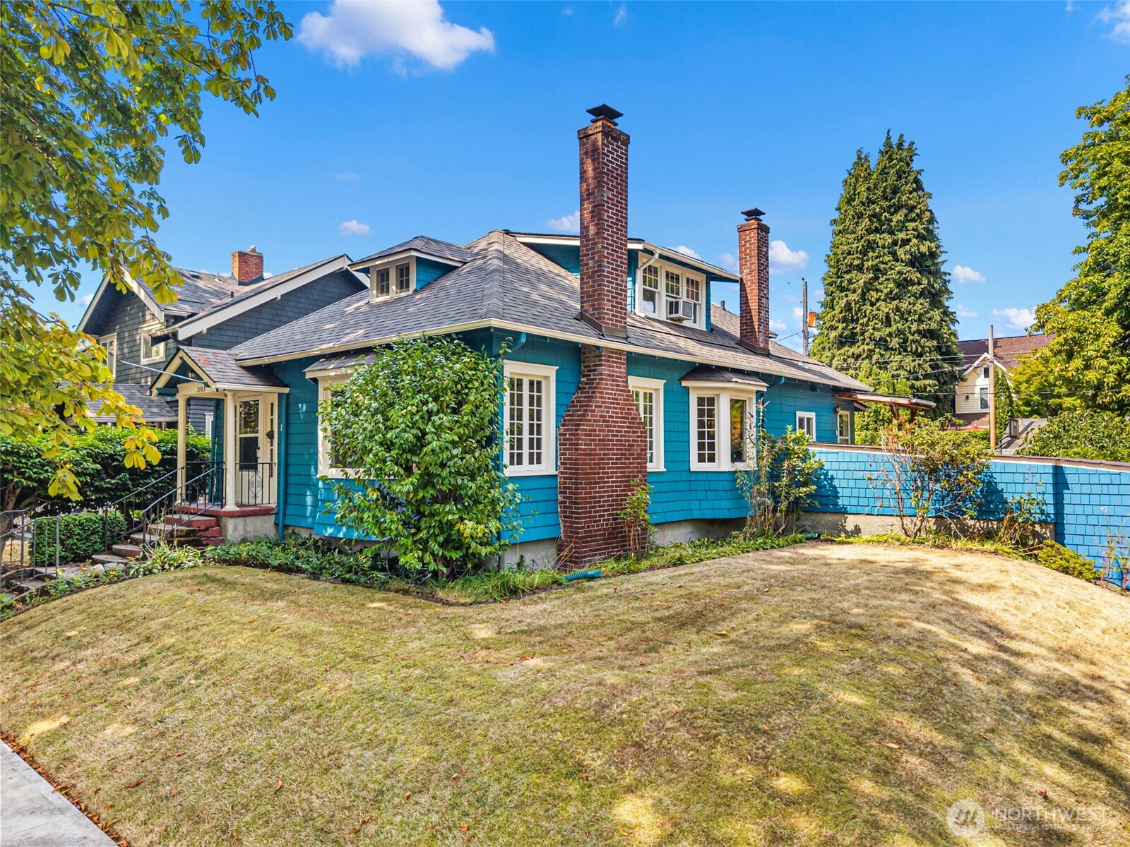 Blue shingle-sided house with white trim, brick chimneys, and a broad front lawn.