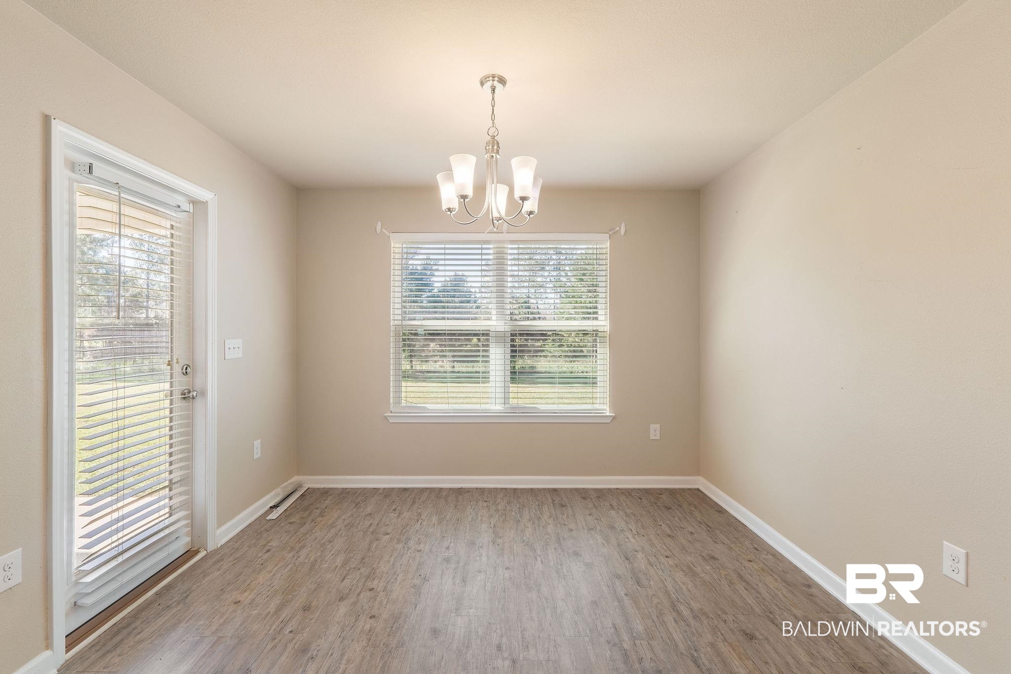 Empty dining room with gray wood-look flooring, a chandelier, and a window with white blinds.