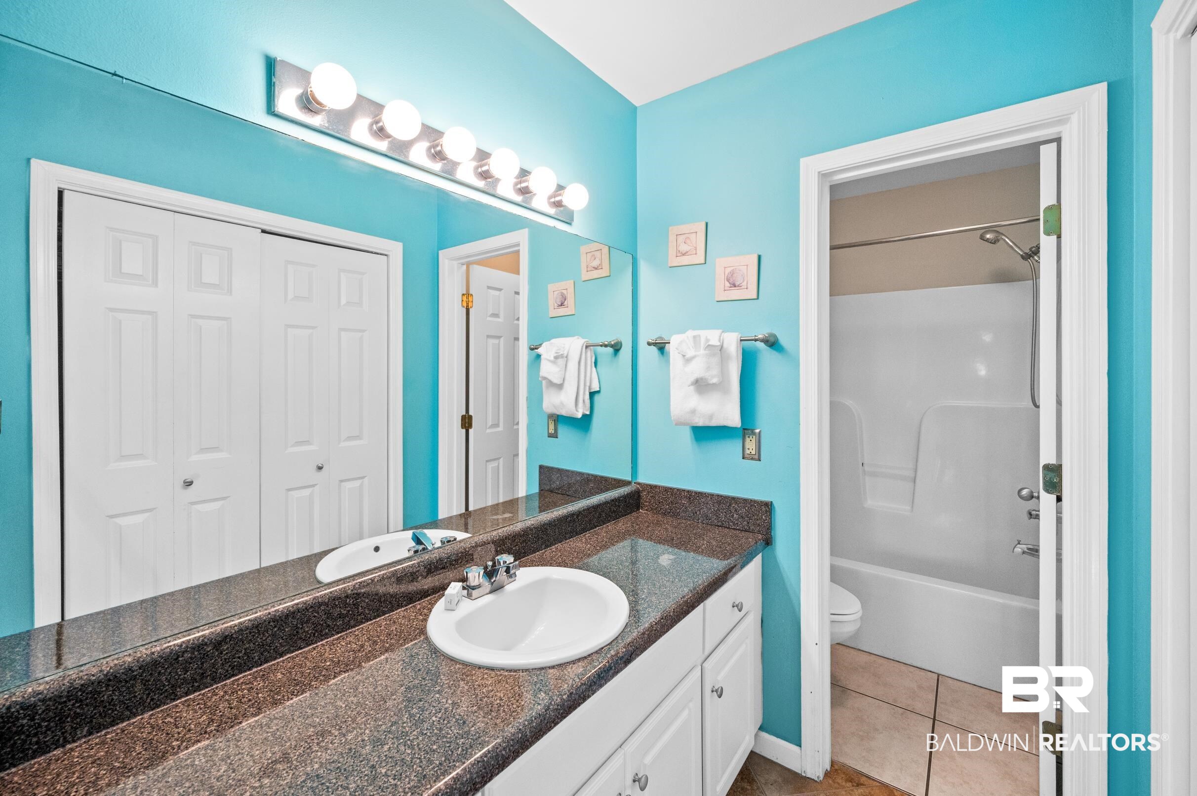 Bathroom with turquoise walls, a granite double vanity, large mirror, and tub-shower combination.