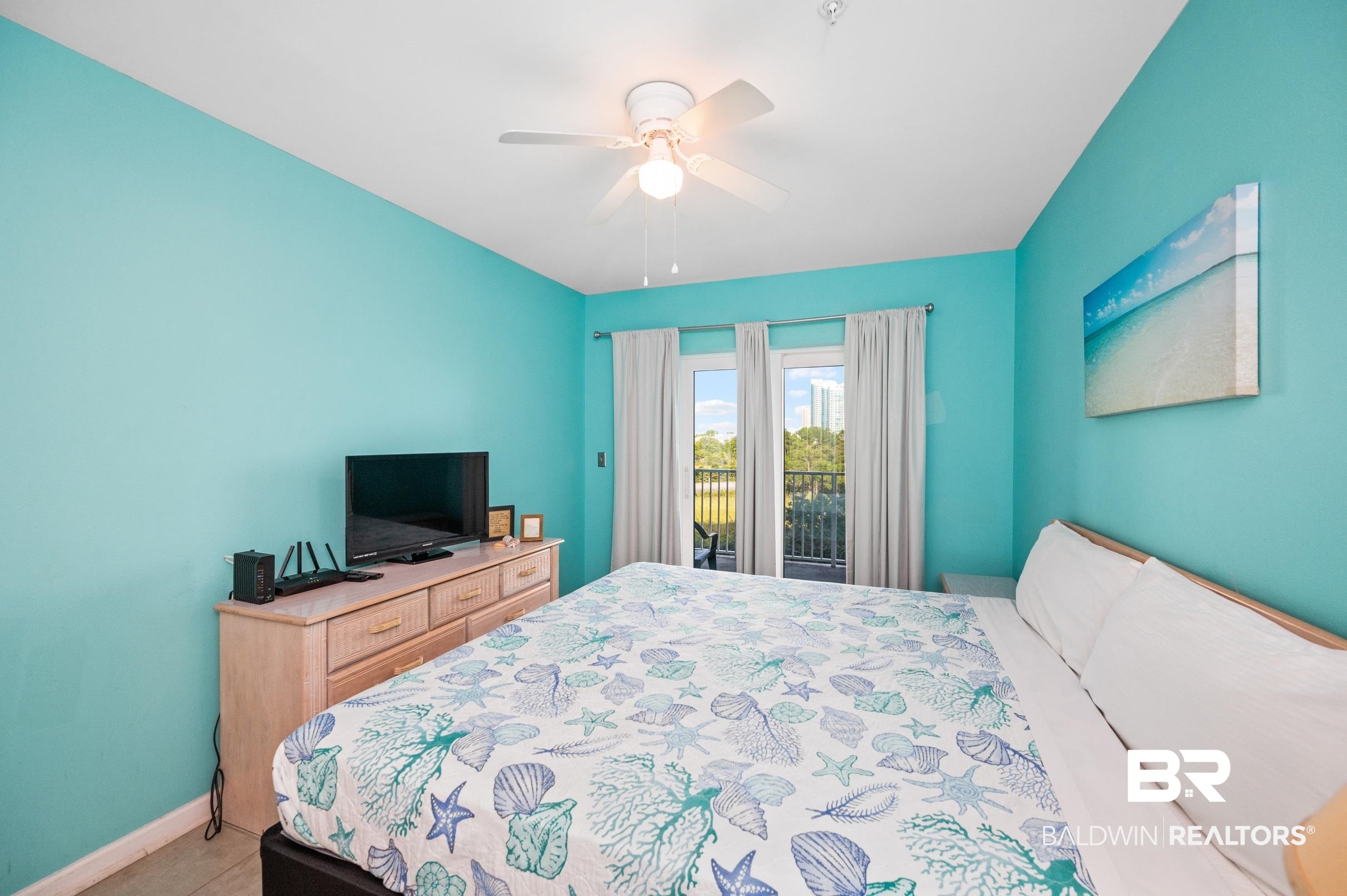 Bedroom with turquoise walls, seashell-patterned bedding, and glass doors opening to a balcony.