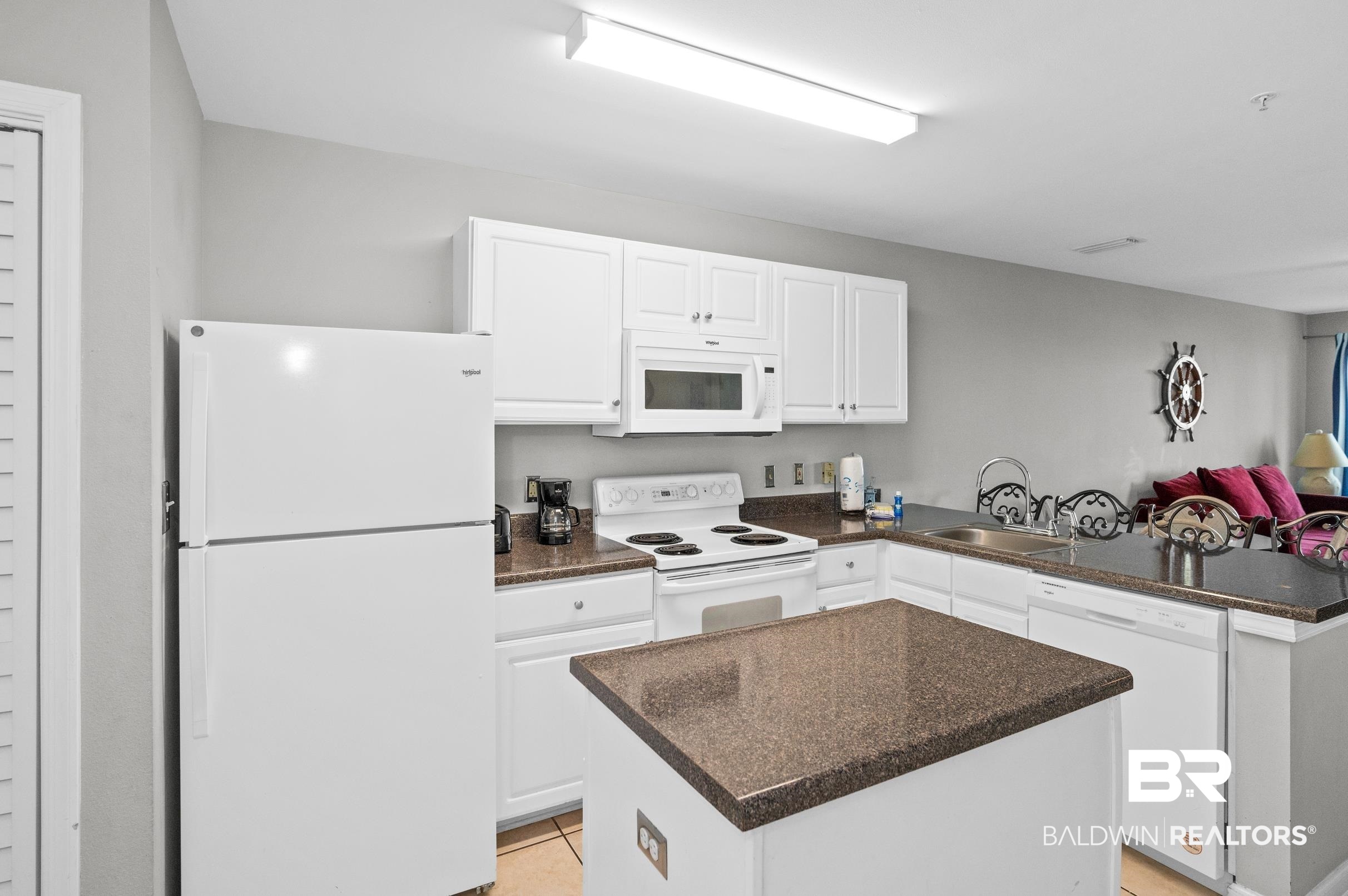Condominium kitchen with white appliances, brown granite counters, and a large island.