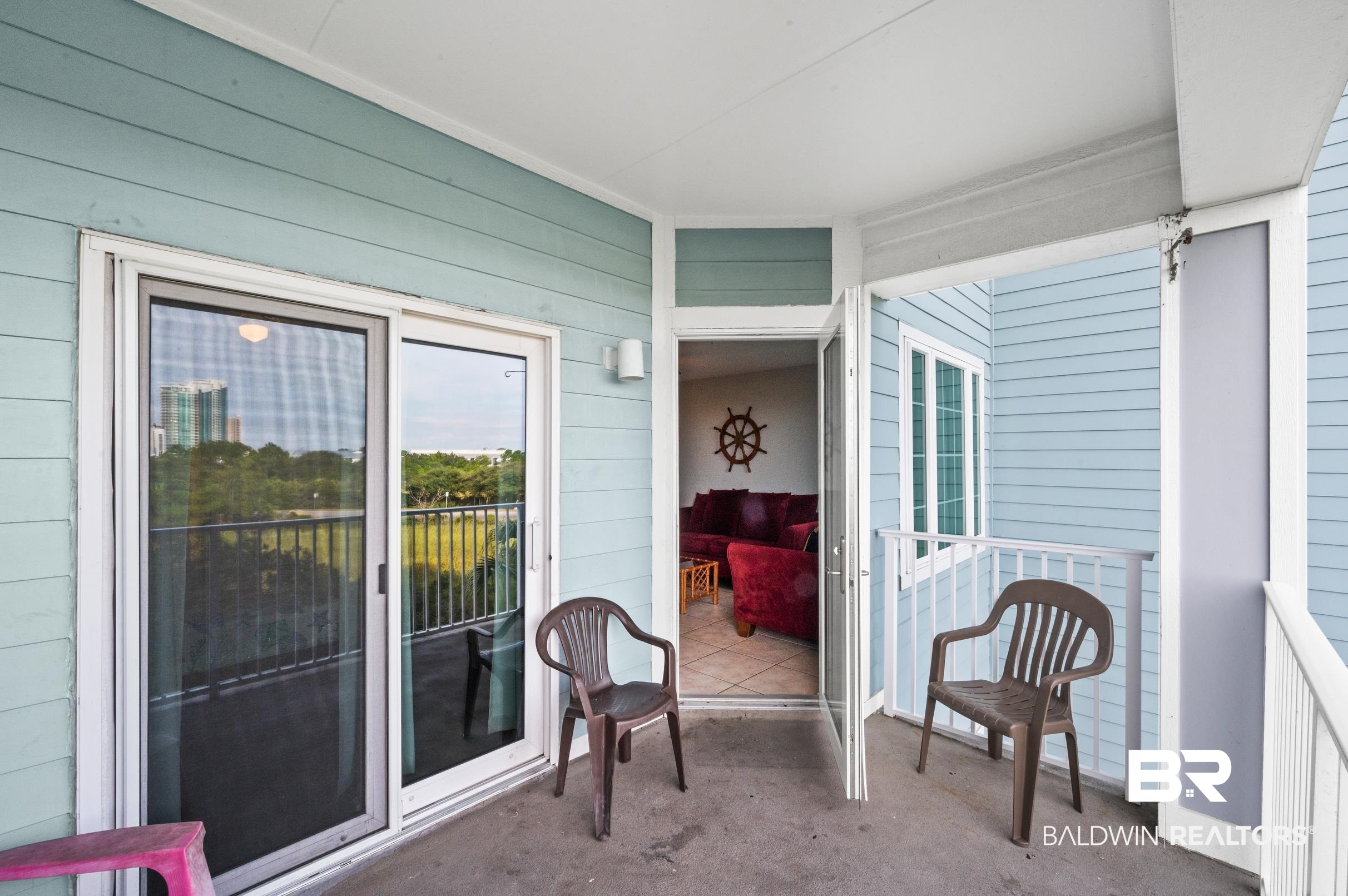 Covered balcony with two chairs and an open doorway to a burgundy-furnished living room.