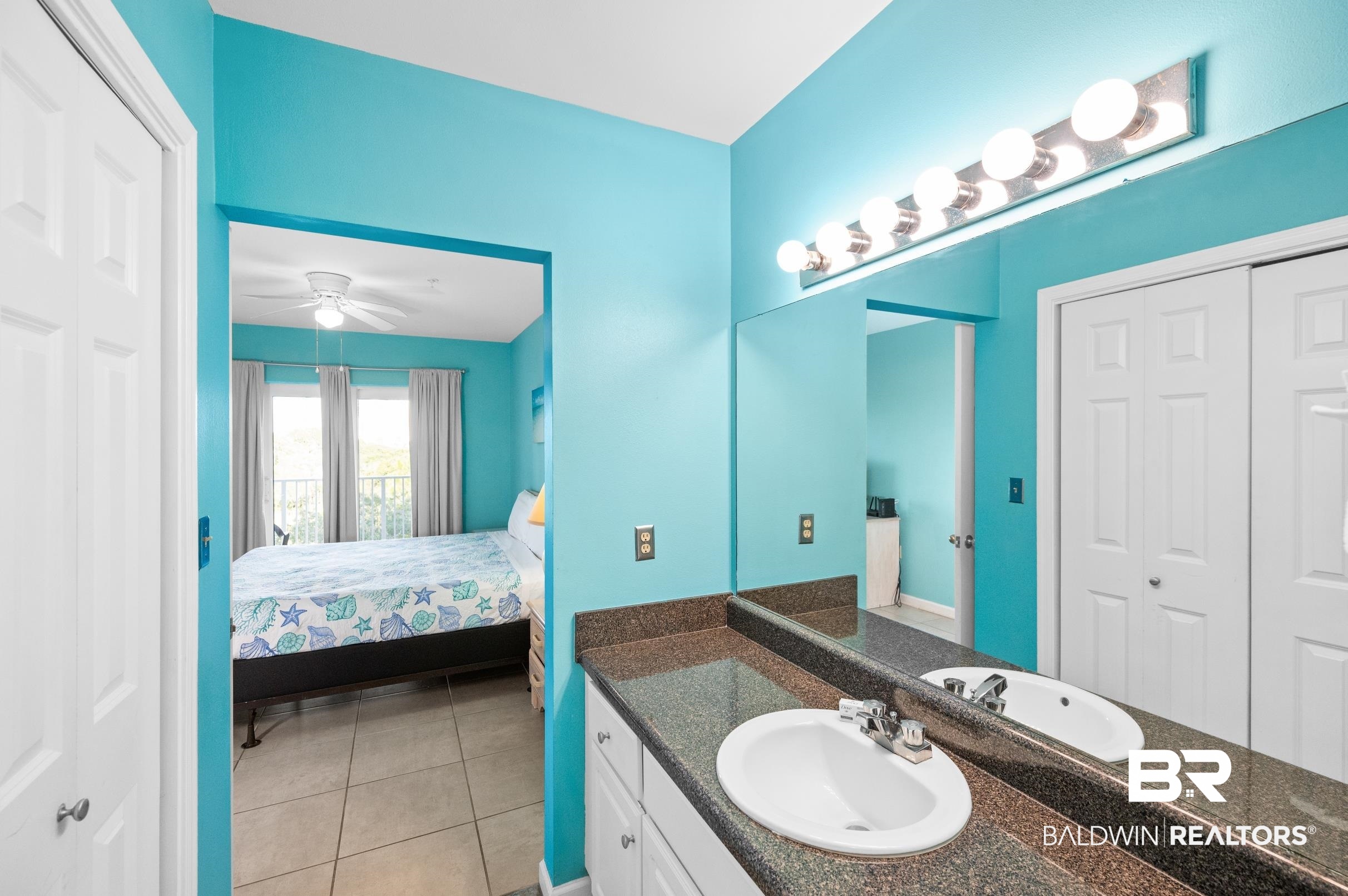 Turquoise bathroom vanity looking into a bedroom with a sea-life patterned bedspread.