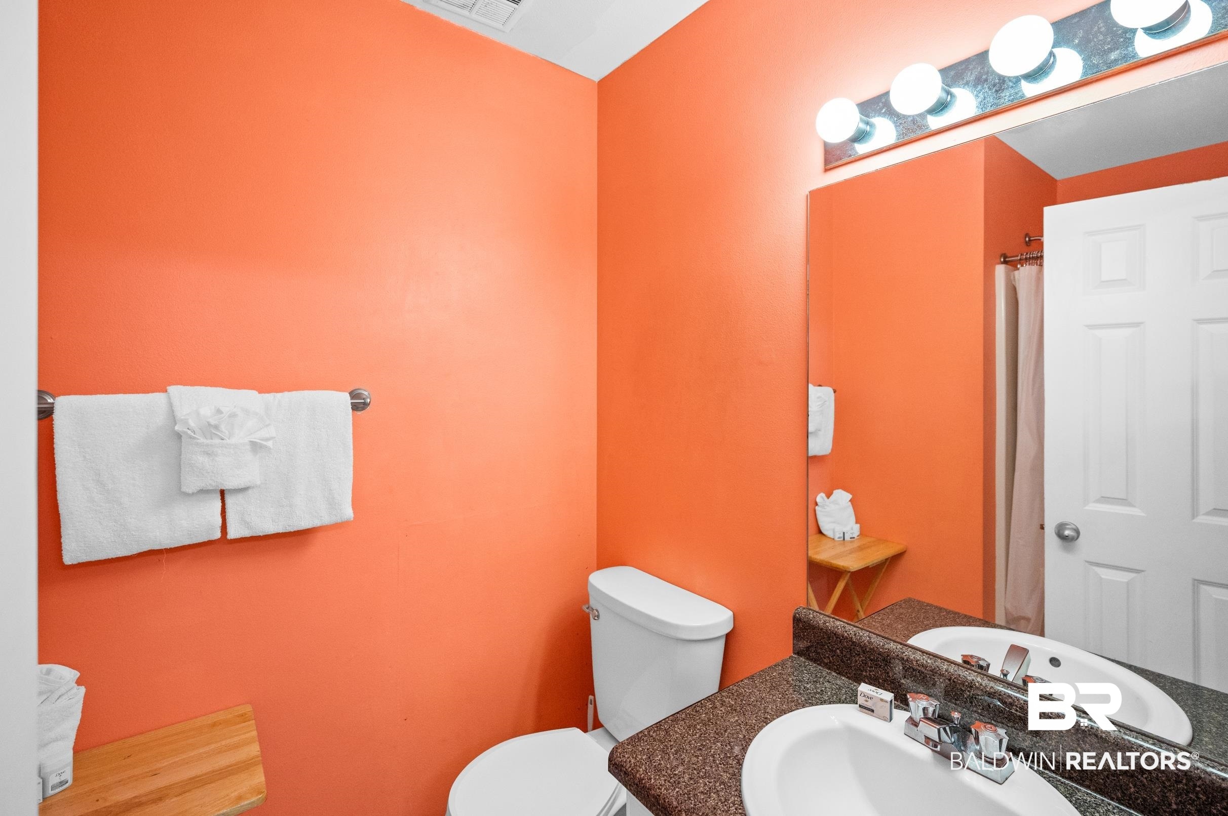 Bathroom with vivid orange walls, a granite vanity, large mirror, and white towels.