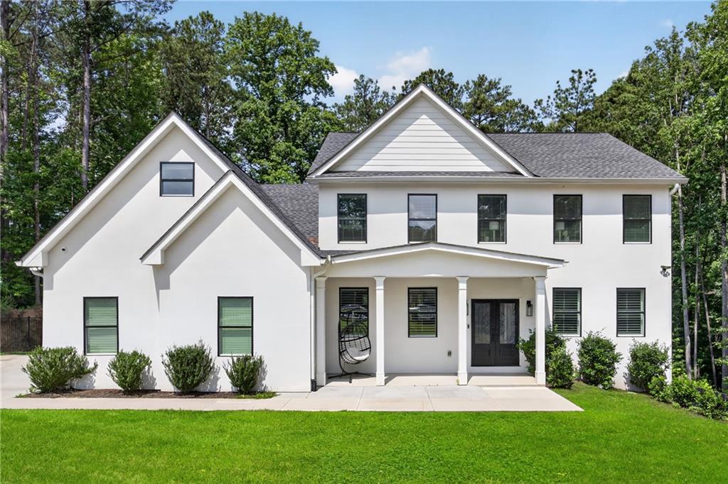 White two-story house with a covered porch and hanging chair, set among trees.