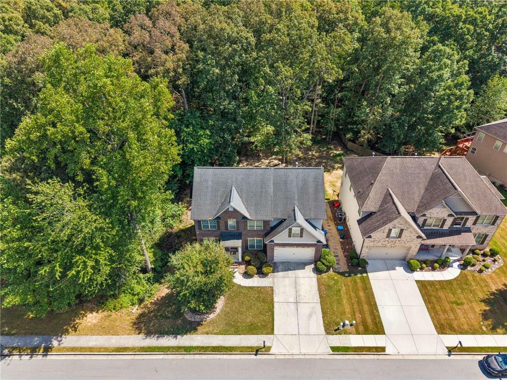 Aerial view of a two-story brick home beside a densely wooded backyard.