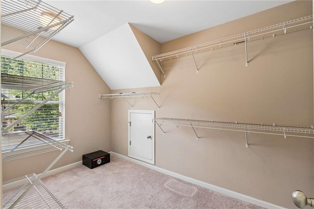 Walk-in closet with extensive wire shelving, beige carpet, and a window with blinds.