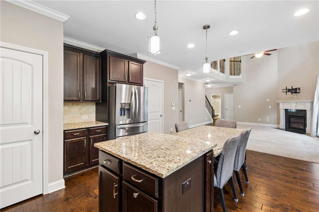 Kitchen with a granite island, dark wood cabinets, stainless steel appliances, and an adjoining living room with a fireplace.