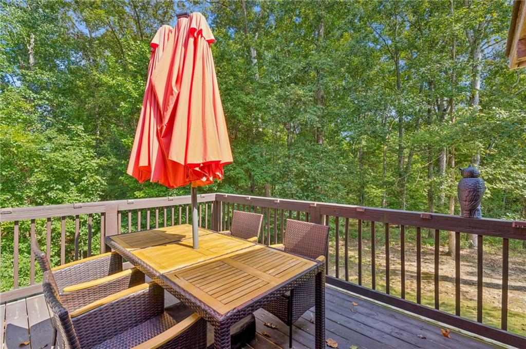 Furnished deck with wicker dining chairs and a red umbrella overlooking trees.