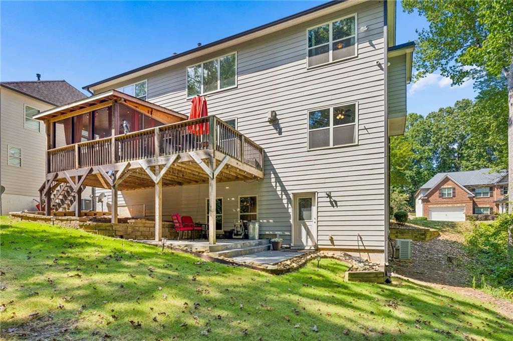 Rear of a two-story home with a raised deck, covered seating area, and sloping lawn.