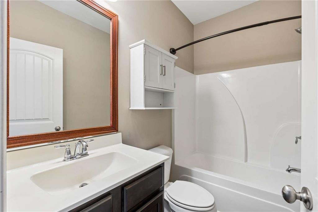 Bathroom with a wood-framed mirror, white vanity, toilet, and tub-shower enclosure.