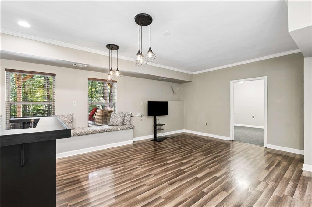 Open living area with wood-look floors, a window bench, pendant lights, and a television.