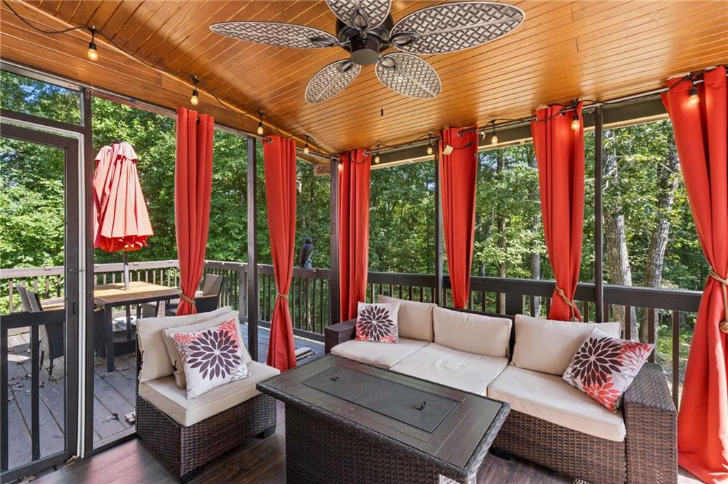 Screened porch with wicker seating, red curtains, a wood ceiling, and a leafy wooded view.