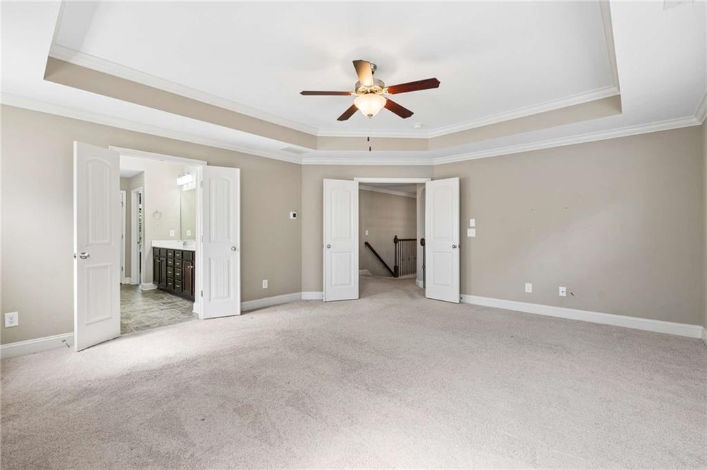 Empty bedroom with a tray ceiling, ceiling fan, and doors to a bathroom and hallway.