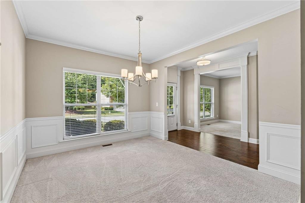 Unfurnished dining room with a chandelier, white wainscoting, and a large window overlooking greenery.