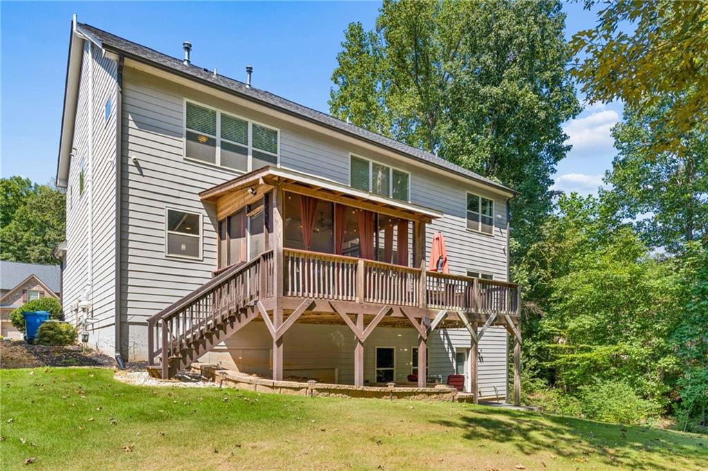 Two-story house with a raised covered wooden deck overlooking a sloped lawn and mature trees.