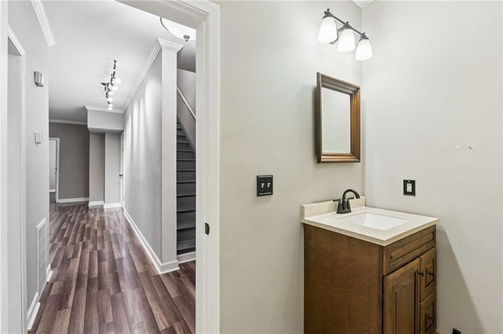 Bathroom vanity beside a hallway with dark plank flooring and a staircase.