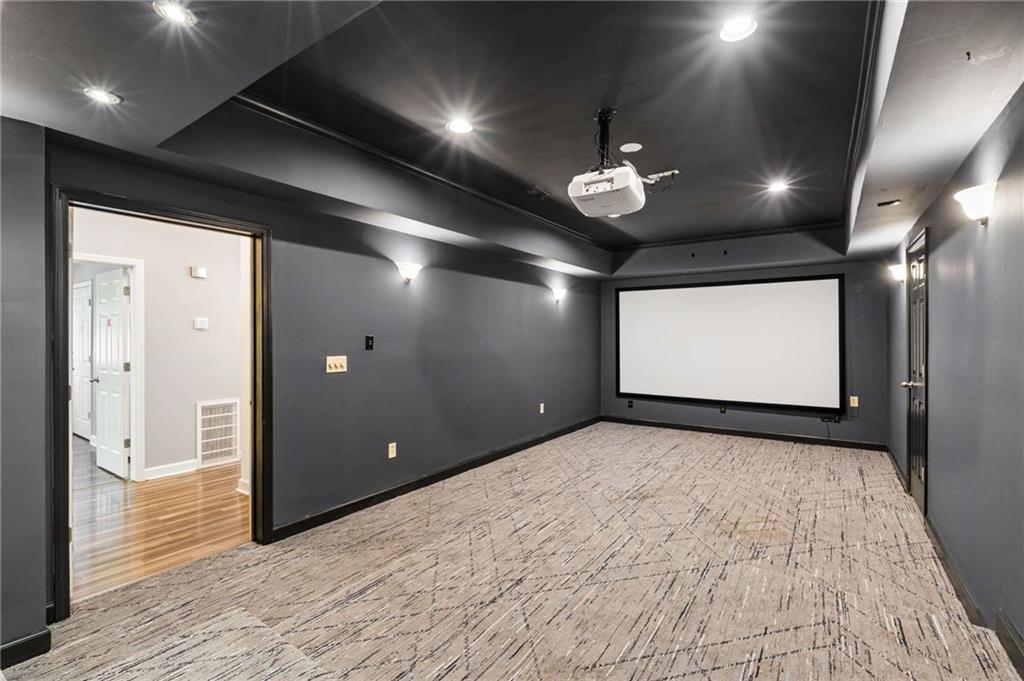 Unfurnished home theater with a large screen, ceiling projector, dark walls, and patterned carpet.