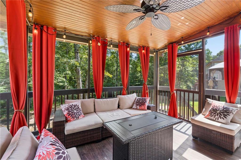 Screened porch with wicker seating, red curtains, and a wood-plank ceiling overlooking trees.