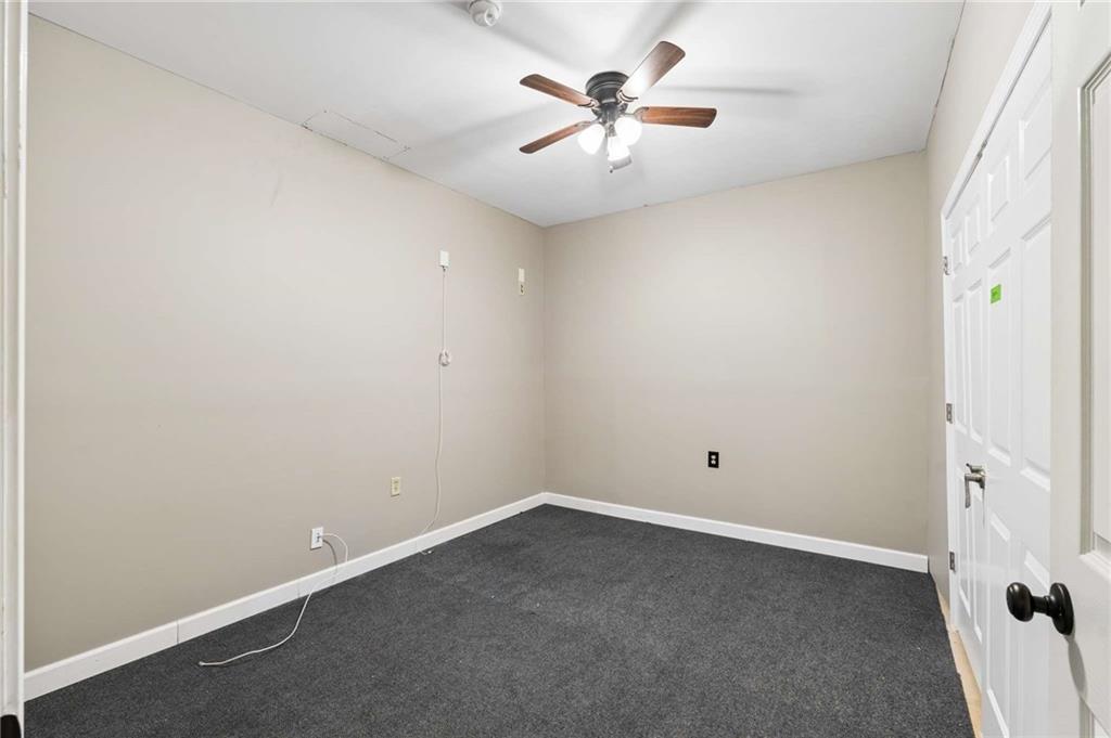 Empty bedroom with dark gray carpet, a ceiling fan, and white closet doors.