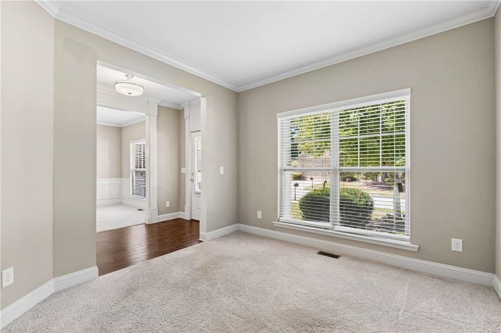 Empty carpeted room with a large window and an open doorway to a room with hardwood floors.