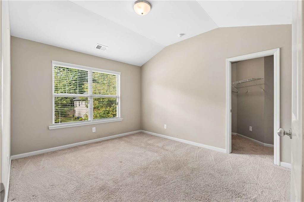 Empty bedroom with beige walls, light carpet, a large blinded window, and an open closet.