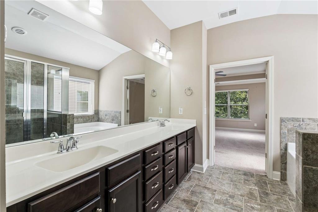 Bathroom with a long double-sink vanity, dark cabinets, and a glass-enclosed tub and shower.