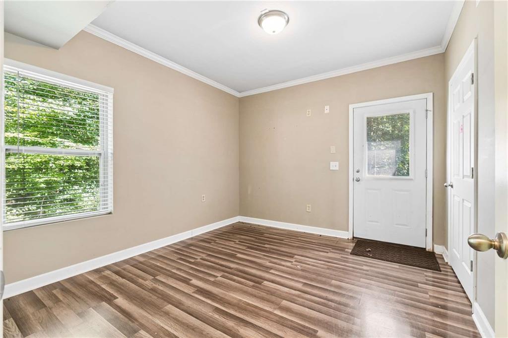 Vacant entry room with wood-look flooring, a window with blinds, and a white exterior door.