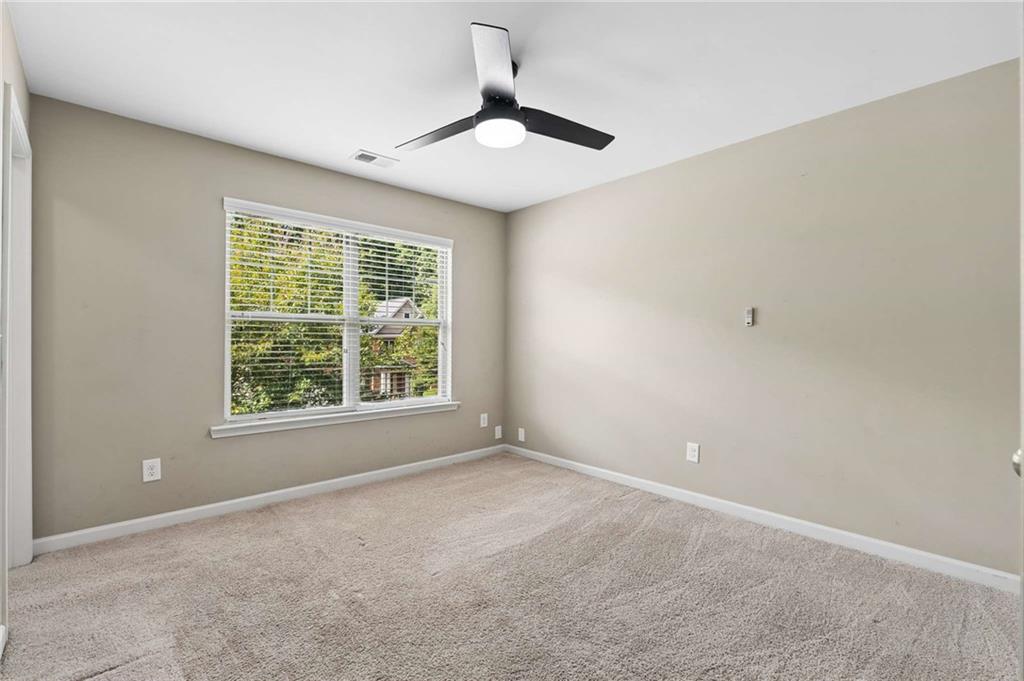 Empty carpeted bedroom with a ceiling fan and a wide window with white blinds.