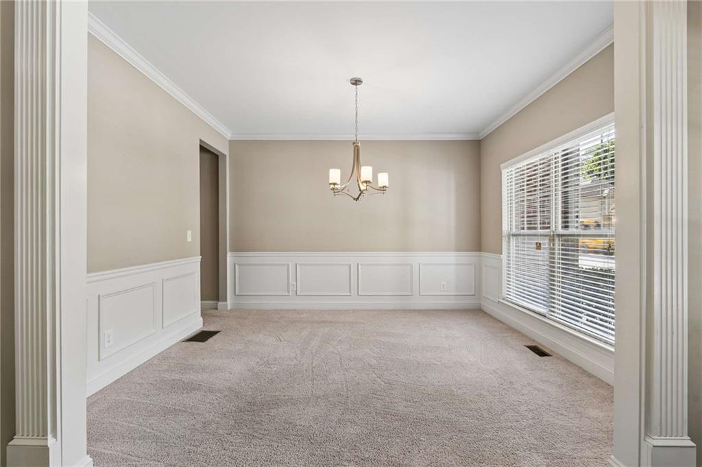 Empty dining room with paneled wainscoting, beige carpet, chandelier, and large window.