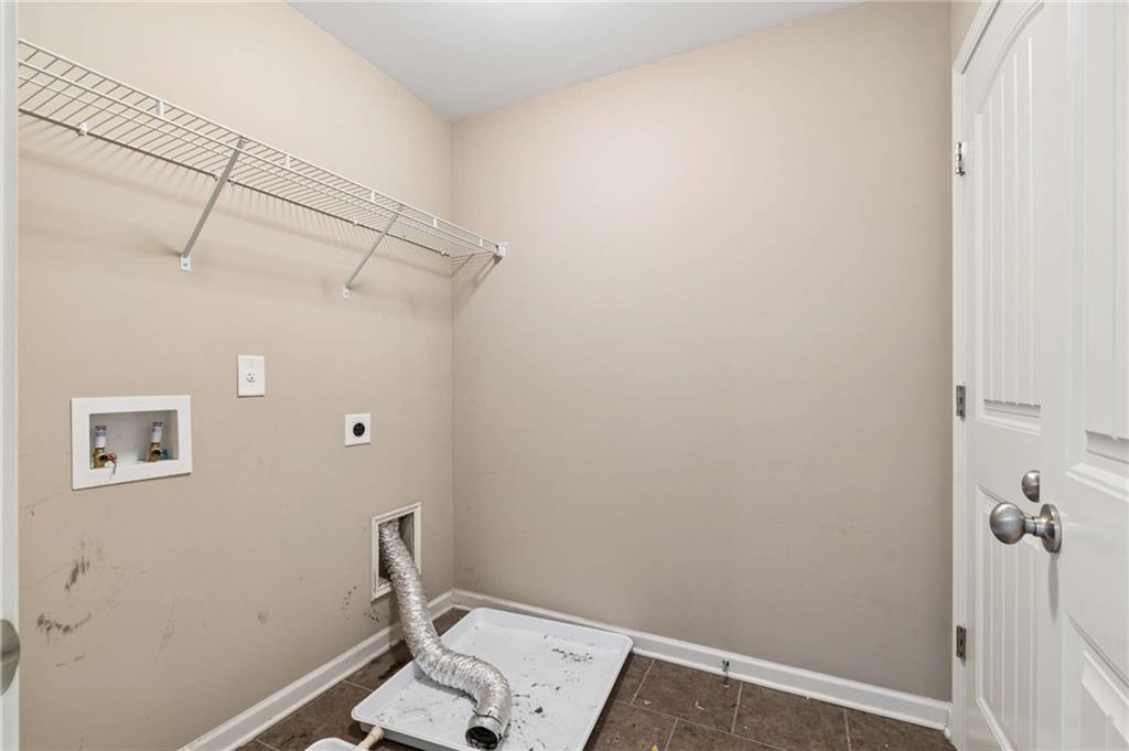 Empty laundry room with washer hookups, dryer vent hose, and wire shelf.