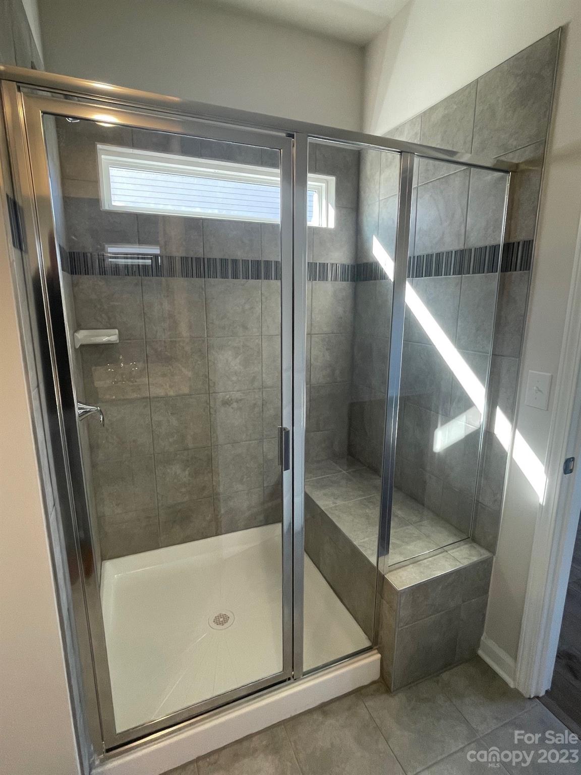 Tiled walk-in shower with glass doors, a built-in bench, and a dark accent stripe.