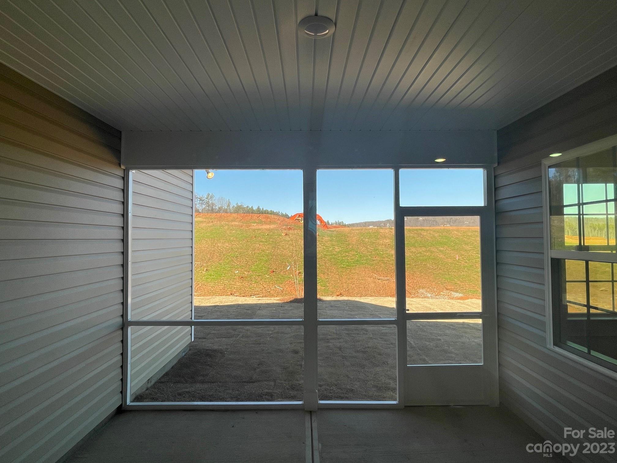 Empty screened porch with gray siding and a view of the graded yard.