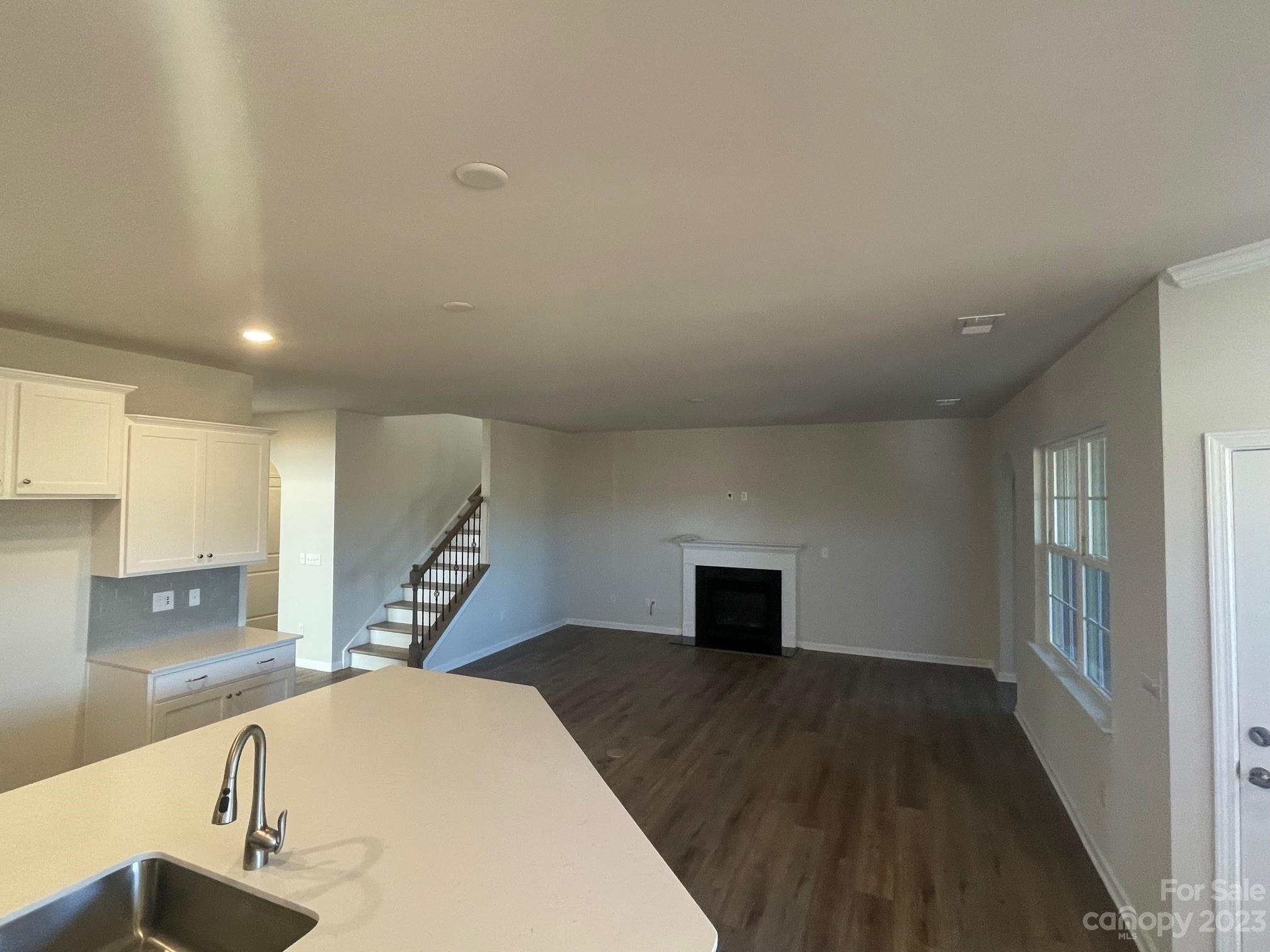 Open-plan kitchen and living room with a large sink peninsula, staircase, and fireplace.