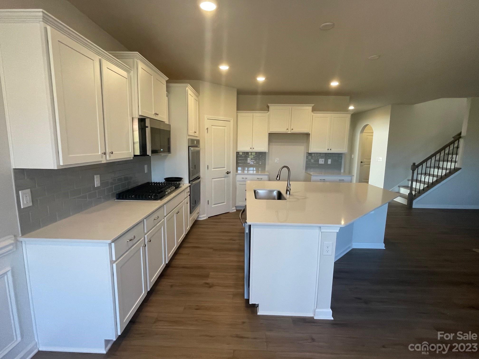 Kitchen with white cabinetry, gray backsplash, gas cooktop, and a large island with an undermount sink.