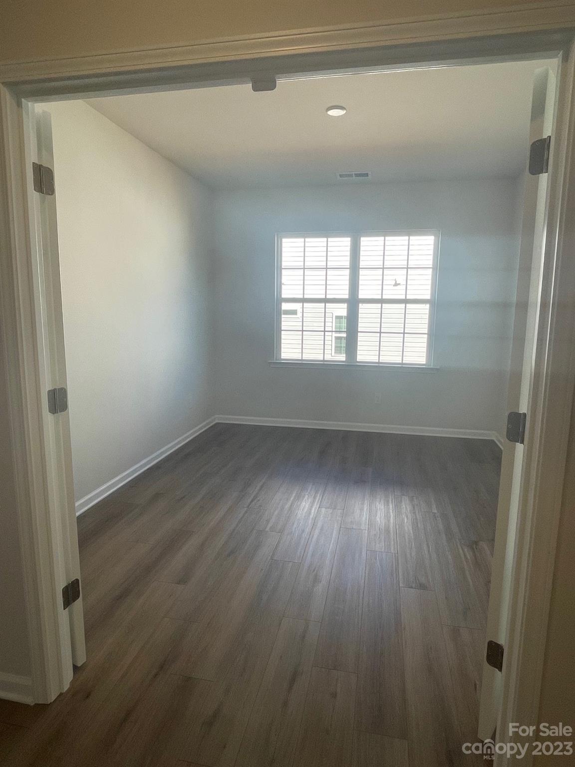 Empty room with plank flooring and a wide window with blinds.