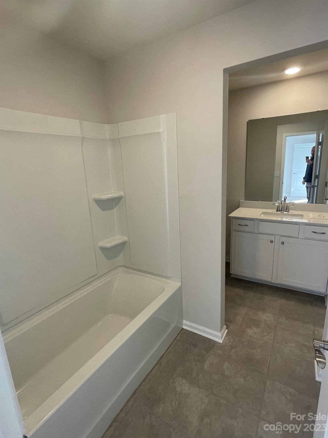 Bathroom with a white tub and molded shower surround, opposite a vanity and large mirror.
