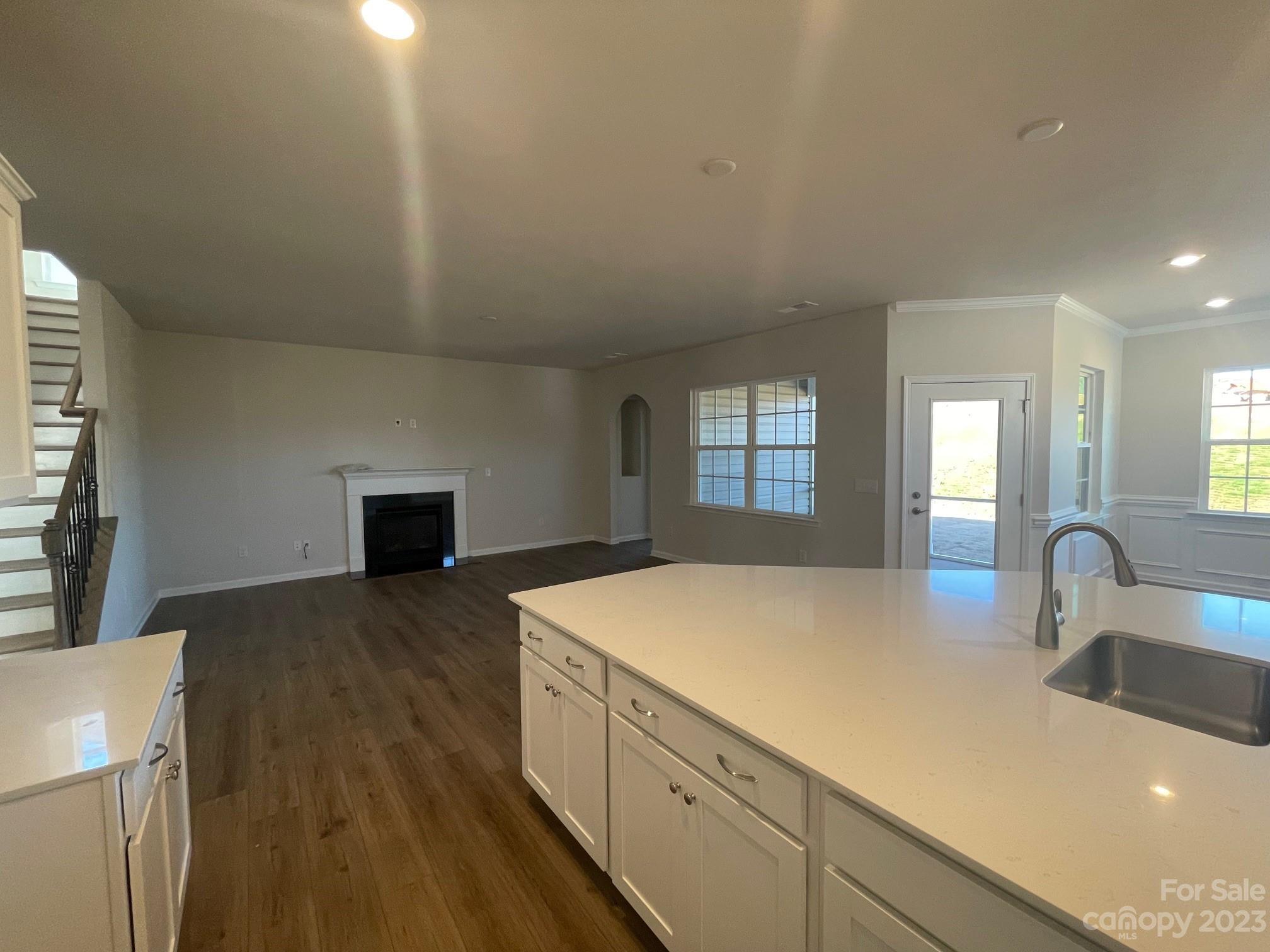 Open kitchen and living room with a large white island, fireplace, and staircase.