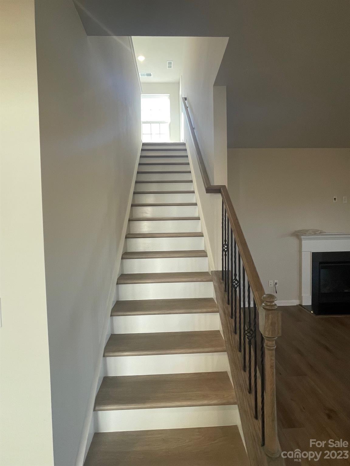 Interior staircase with wood treads, white risers, and dark metal balusters beside a fireplace.