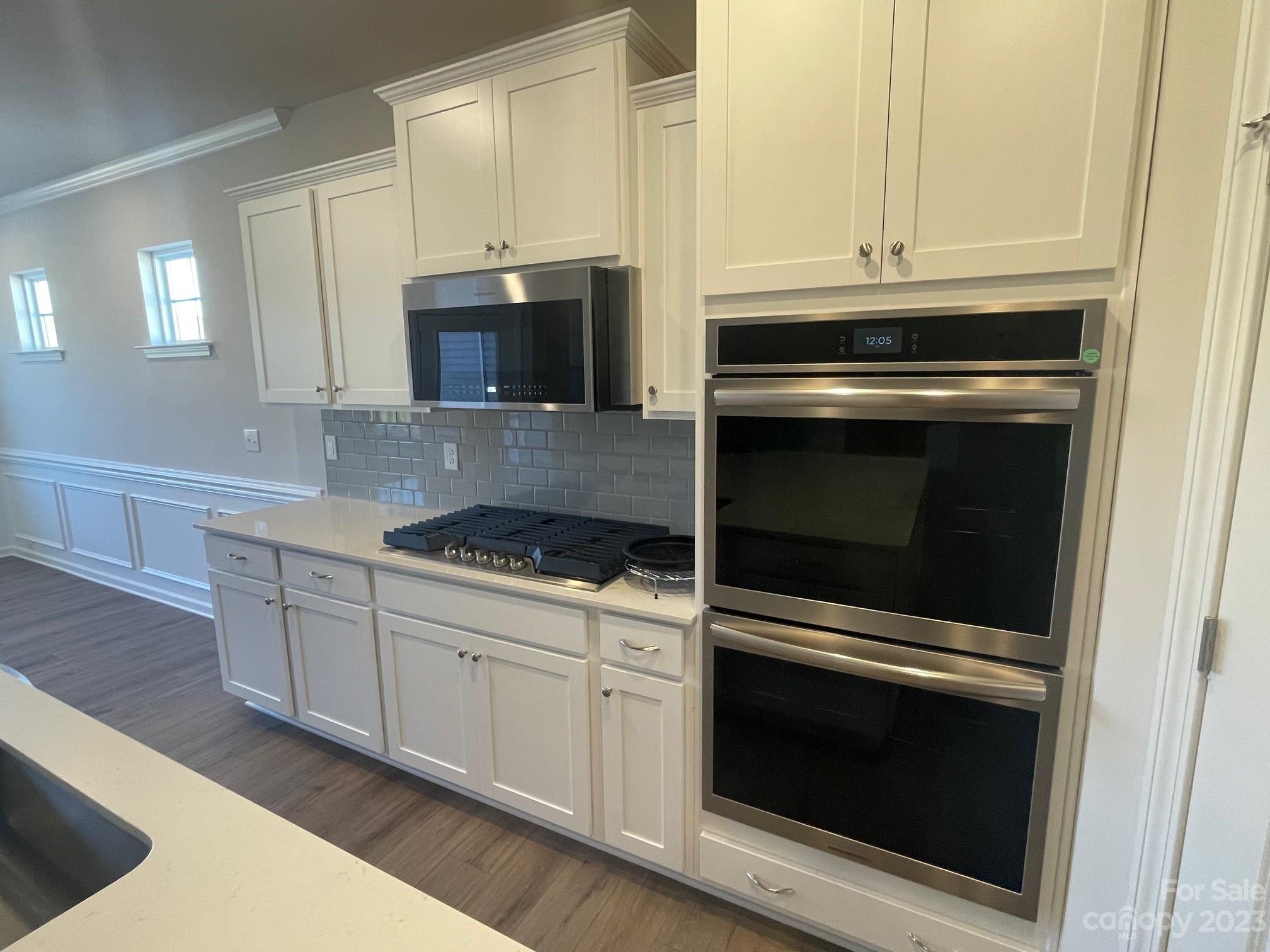 Kitchen with white cabinets, gas cooktop, stainless-steel double ovens, and gray tile backsplash.