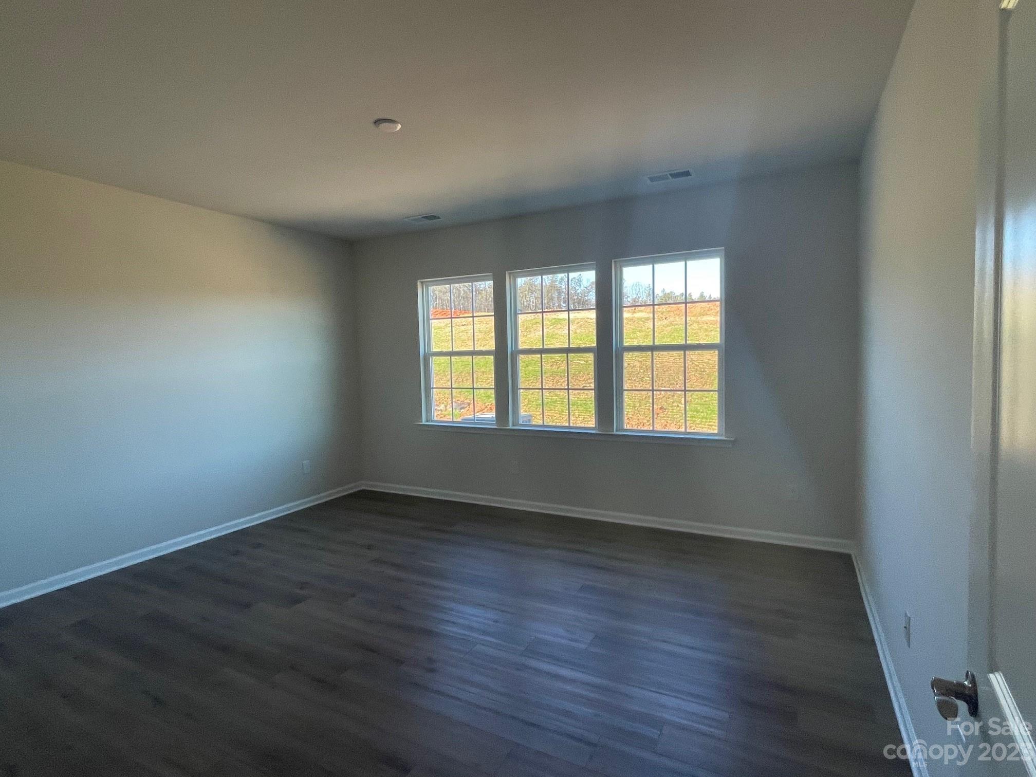 Empty room with dark flooring and three grid-pane windows overlooking a grassy slope.