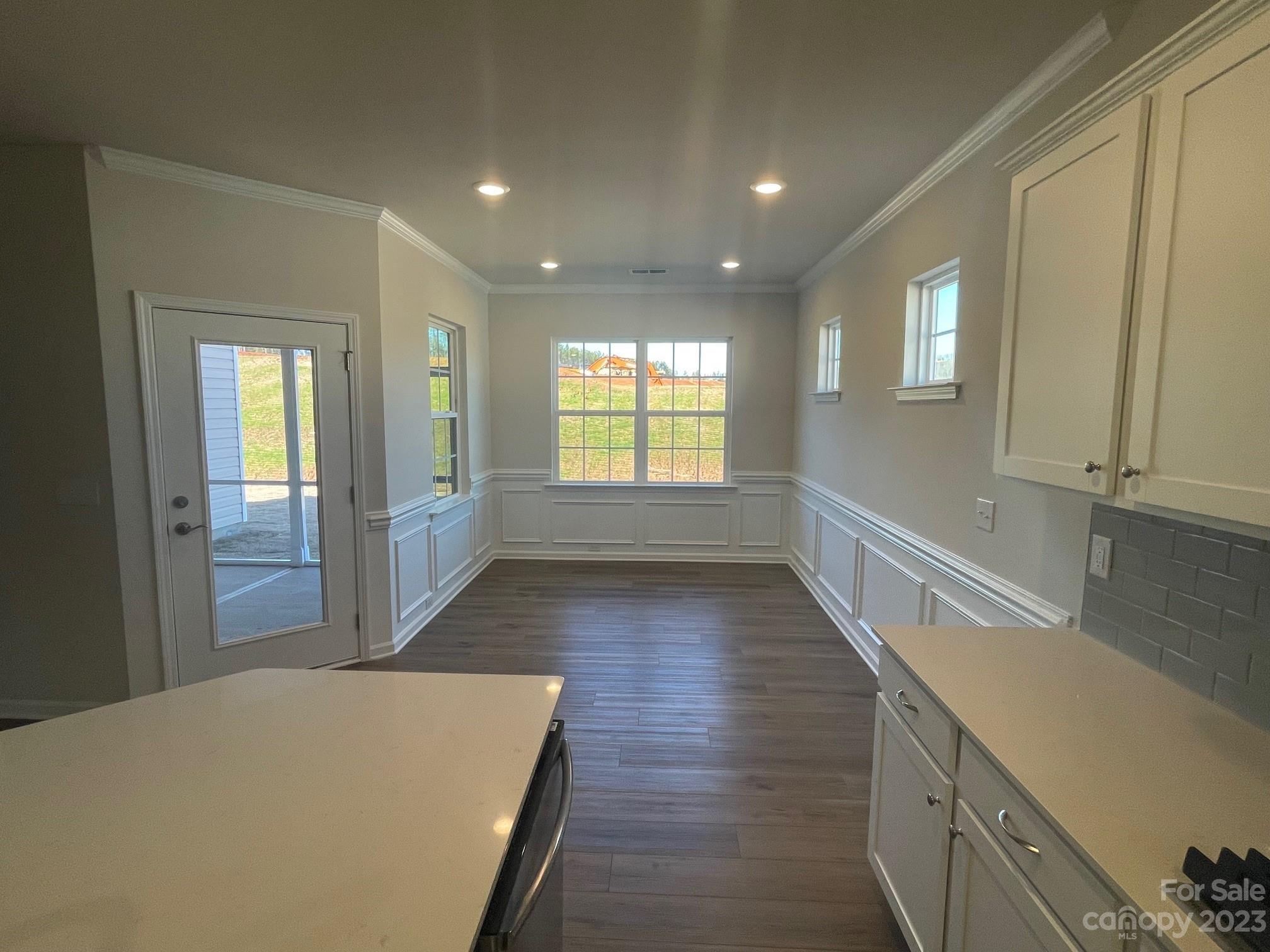 Empty kitchen and dining area with white cabinetry, dark flooring, and a glass-paneled exterior door.