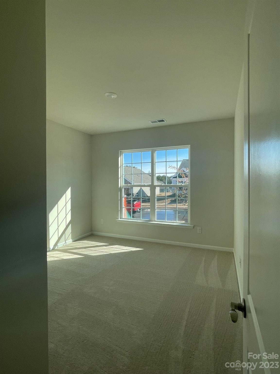 Empty carpeted room with a large divided-pane window and sunlight casting grid shadows on the floor.