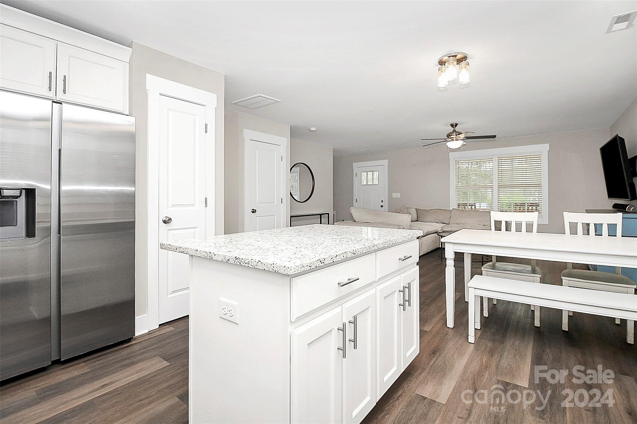 Open-plan kitchen with a large white island, stainless steel refrigerator, dining table, and beige sectional.
